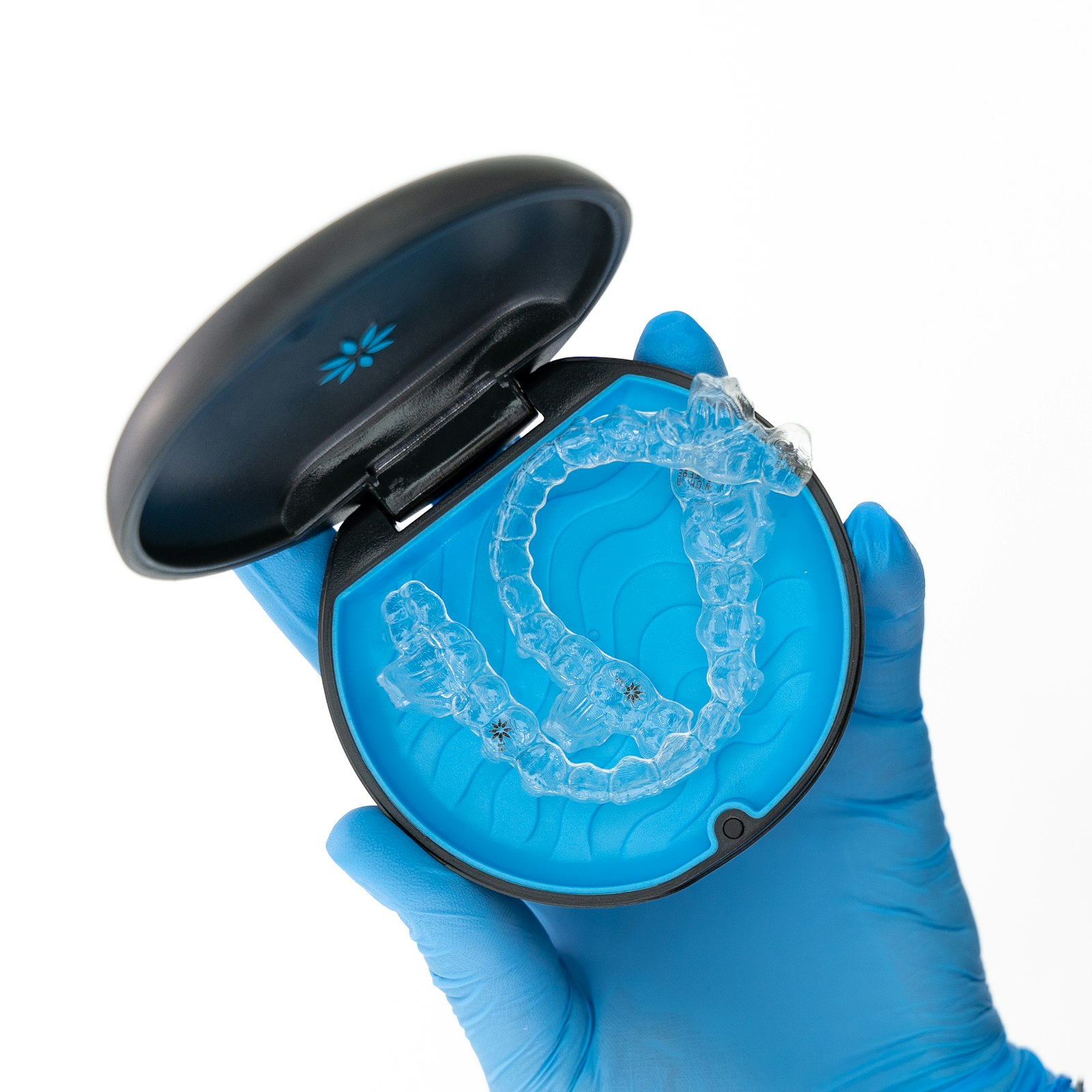 A gloved hand holding an open case with a clear aligner